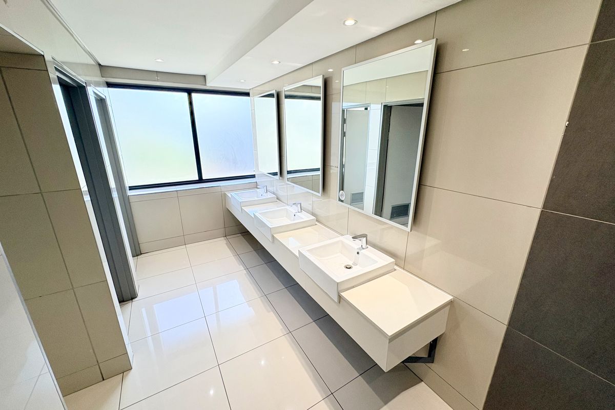 Modern office restroom featuring a triple vanity setup with integrated sinks, large wall-mounted mirrors, and polished floor tiles.