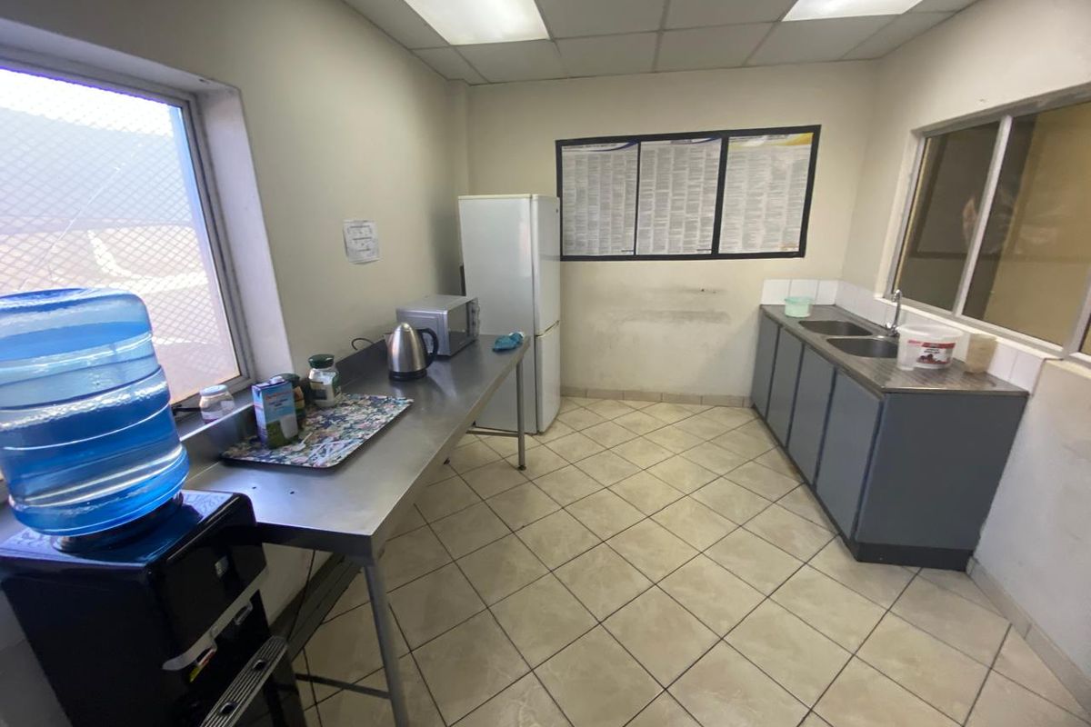 A functional industrial kitchenette featuring stainless steel prep surfaces, a double sink, tiled flooring, and recessed ceiling lighting.