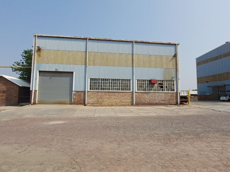 Industrial warehouse exterior featuring metal cladding, a large roller shutter door, and brick base, situated within a paved industrial yard.