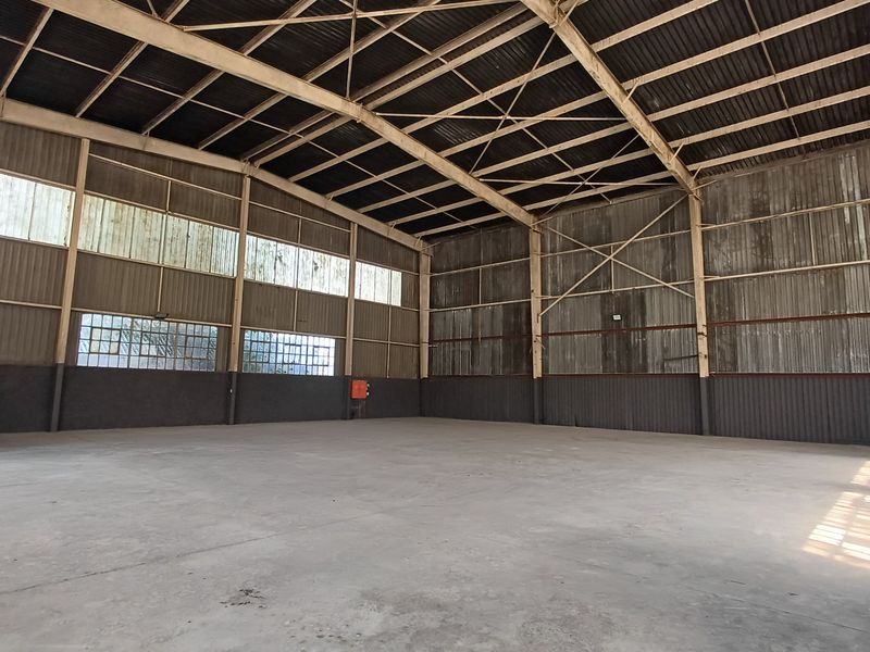 Spacious industrial warehouse featuring high ceilings with exposed steel trusses, concrete flooring, and corrugated metal wall cladding with clerestory windows.