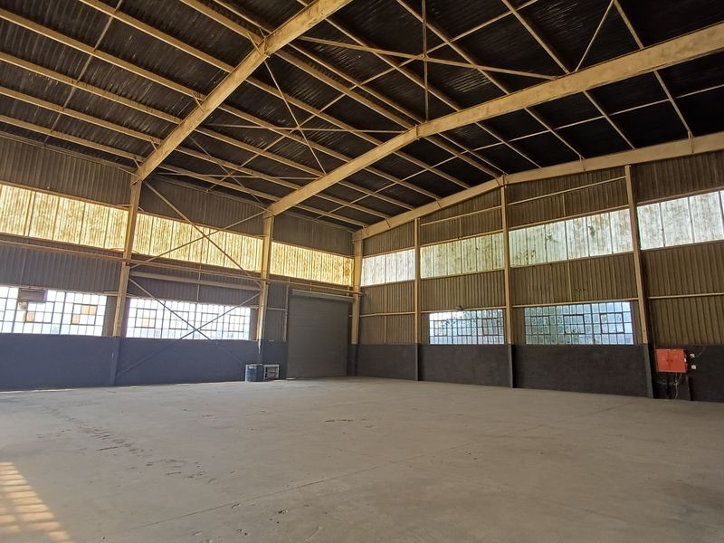 Spacious industrial warehouse featuring high ceilings, exposed steel trusses, concrete flooring, and large clerestory windows providing ample natural light.