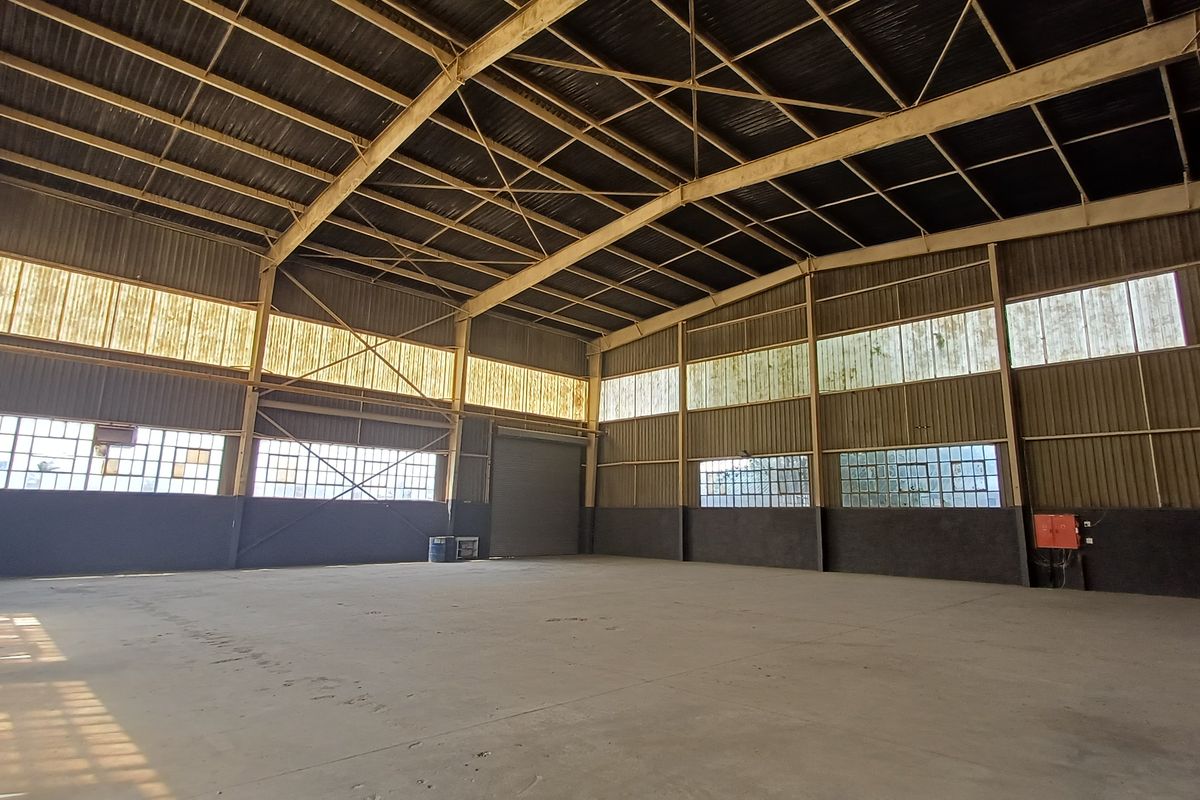 Spacious industrial warehouse featuring high ceilings, exposed steel trusses, concrete flooring, and large clerestory windows providing ample natural light.