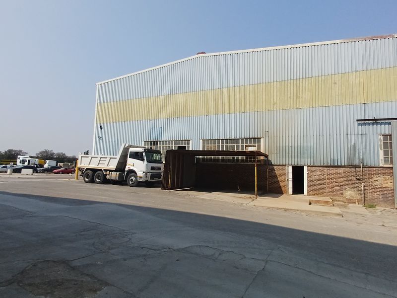 Industrial warehouse exterior featuring corrugated metal cladding, brick masonry base, and a large concrete yard area suitable for heavy vehicle access.