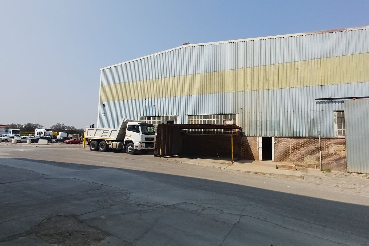 Industrial warehouse exterior featuring corrugated metal cladding, brick masonry base, and a large concrete yard area suitable for heavy vehicle access.
