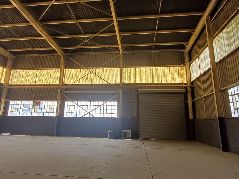 Spacious industrial warehouse unit featuring a high-clearance steel portal frame, concrete flooring, roller shutter access, and ample natural light through translucent panels.