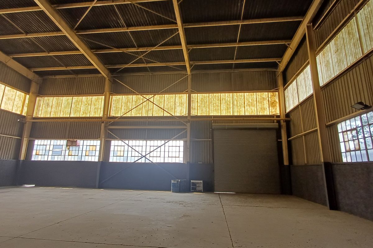 Spacious industrial warehouse unit featuring a high-clearance steel portal frame, concrete flooring, roller shutter access, and ample natural light through translucent panels.