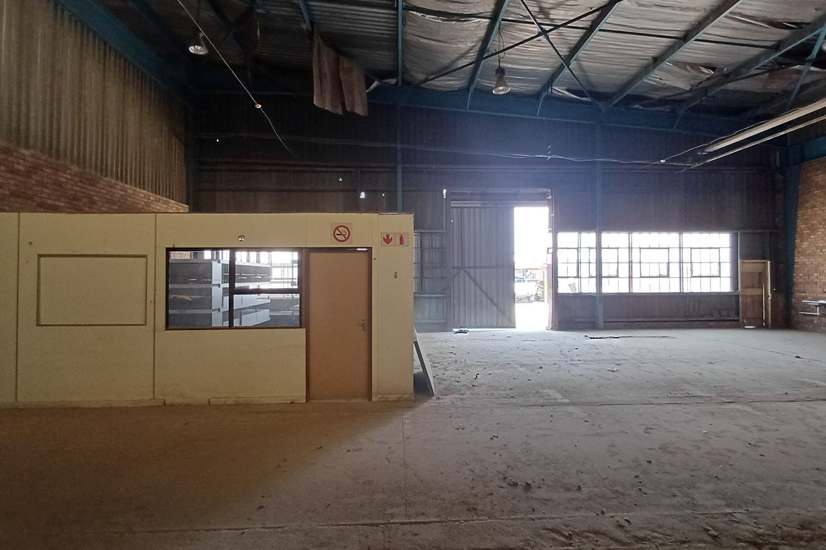 Spacious industrial warehouse featuring high ceilings, exposed brick walls, concrete flooring, and a partitioned office enclosure with large windows.