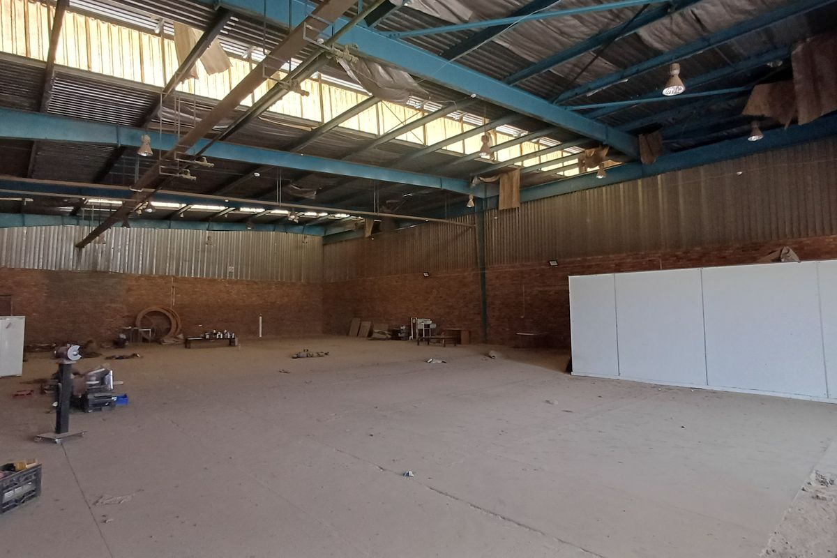Spacious industrial warehouse featuring high-clearance ceilings, exposed steel trusses, brick walls, and concrete flooring, suitable for various commercial or storage applications.