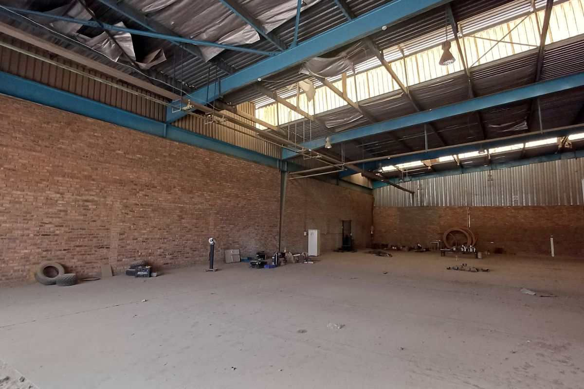 Spacious industrial warehouse featuring high ceilings, exposed brick walls, and concrete flooring, suitable for storage or manufacturing operations.