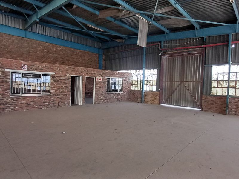 Spacious industrial utility area featuring exposed brick walls, high steel roof trusses, concrete flooring, and large industrial sliding access doors.