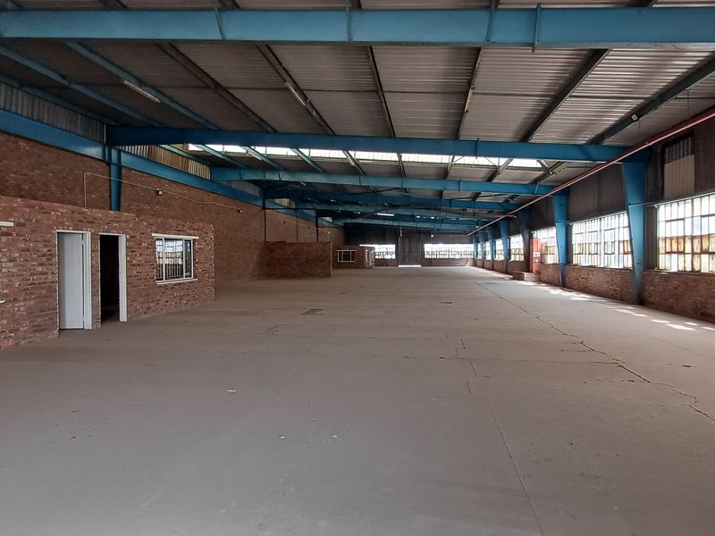 Expansive industrial warehouse space featuring exposed steel trusses, brick walls, and large steel-framed windows, offering a versatile open-plan layout for various commercial operations.
