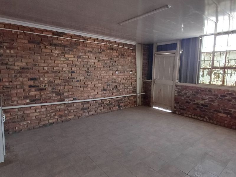 An industrial utility space featuring exposed brick walls, tiled flooring, and large steel-framed windows, offering a functional area for storage or workspace.