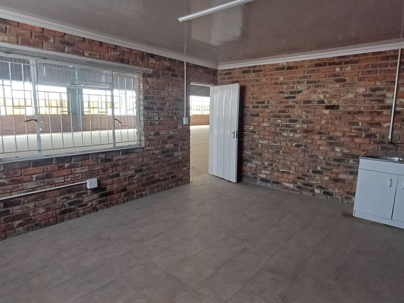 A functional utility space featuring exposed brick walls, tiled flooring, and a built-in sink cabinet, suitable for office or workshop use.