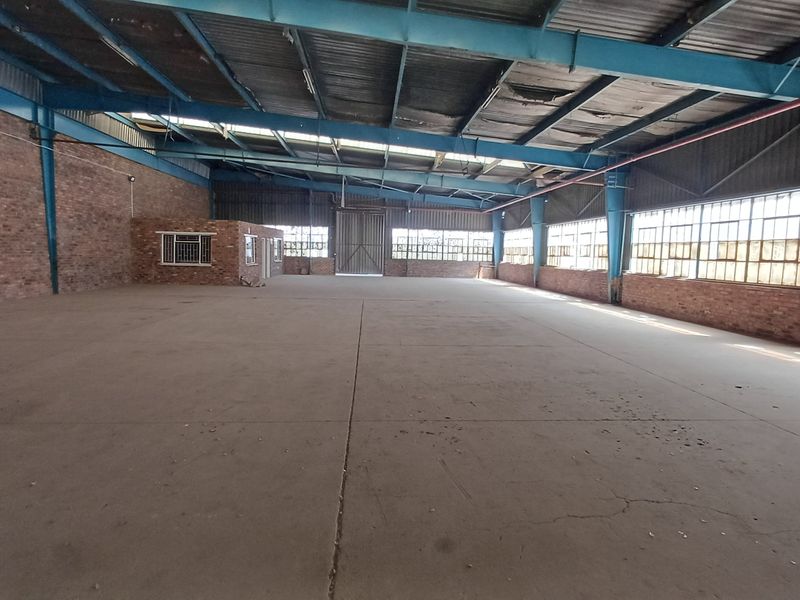 Expansive industrial warehouse space featuring exposed steel trusses, concrete flooring, and large steel-framed windows, offering a versatile open-plan layout.