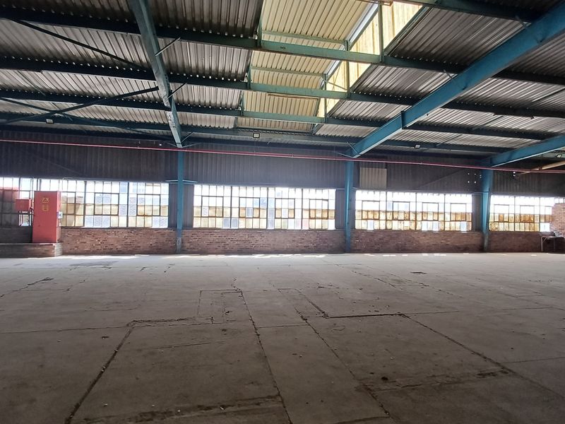 Spacious industrial warehouse featuring high ceilings with exposed steel trusses, large multi-pane windows, and durable concrete flooring, suitable for various commercial or storage uses.