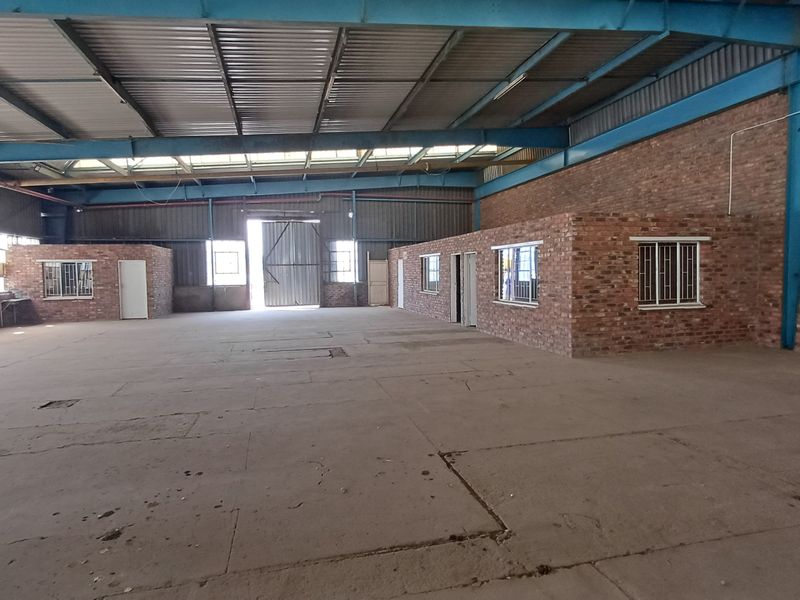 Spacious industrial warehouse featuring exposed steel roof trusses, concrete flooring, and internal brick-built office or utility rooms with secure window bars.