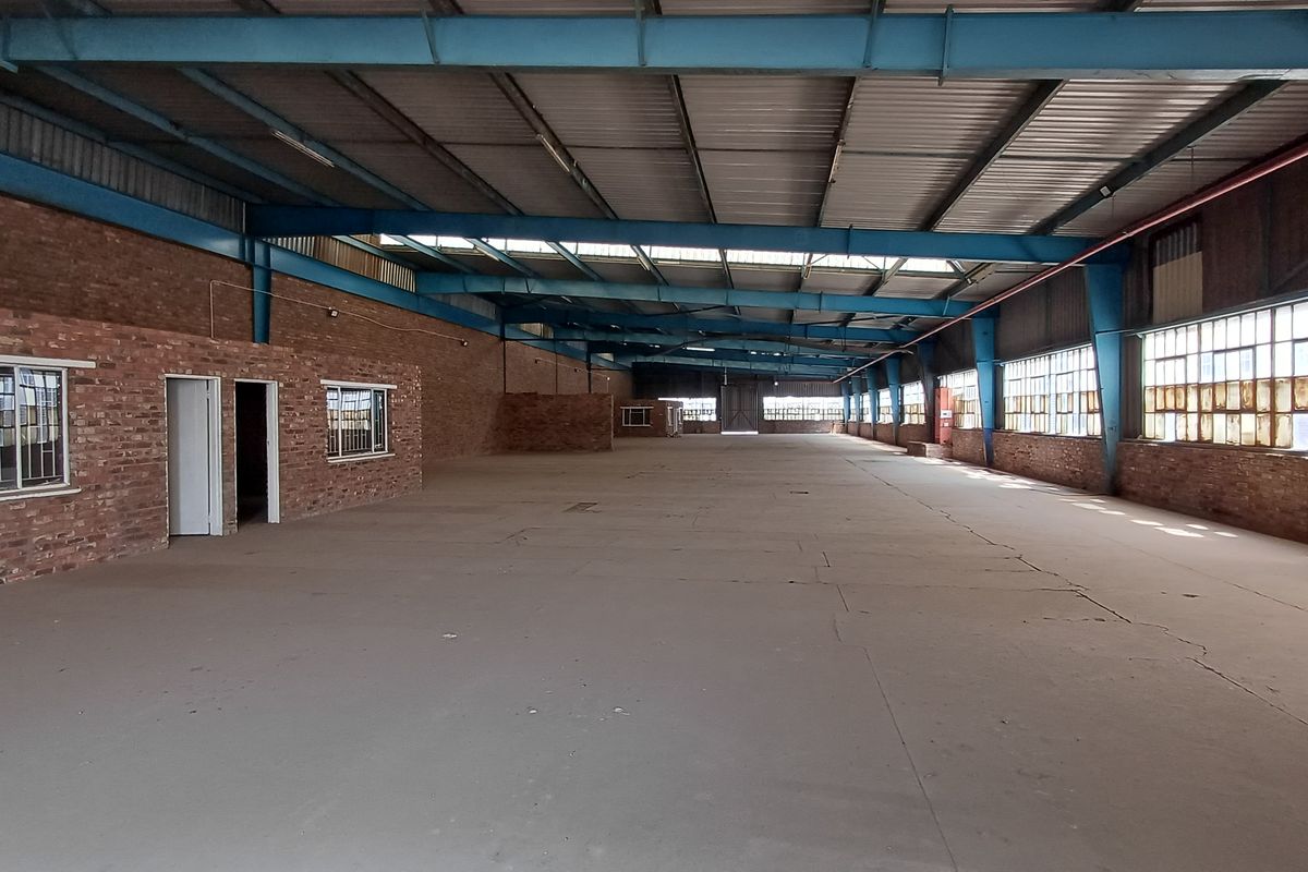 Expansive industrial warehouse space featuring exposed steel trusses, brick walls, and large steel-framed windows, offering a versatile open-plan layout for various commercial operations.