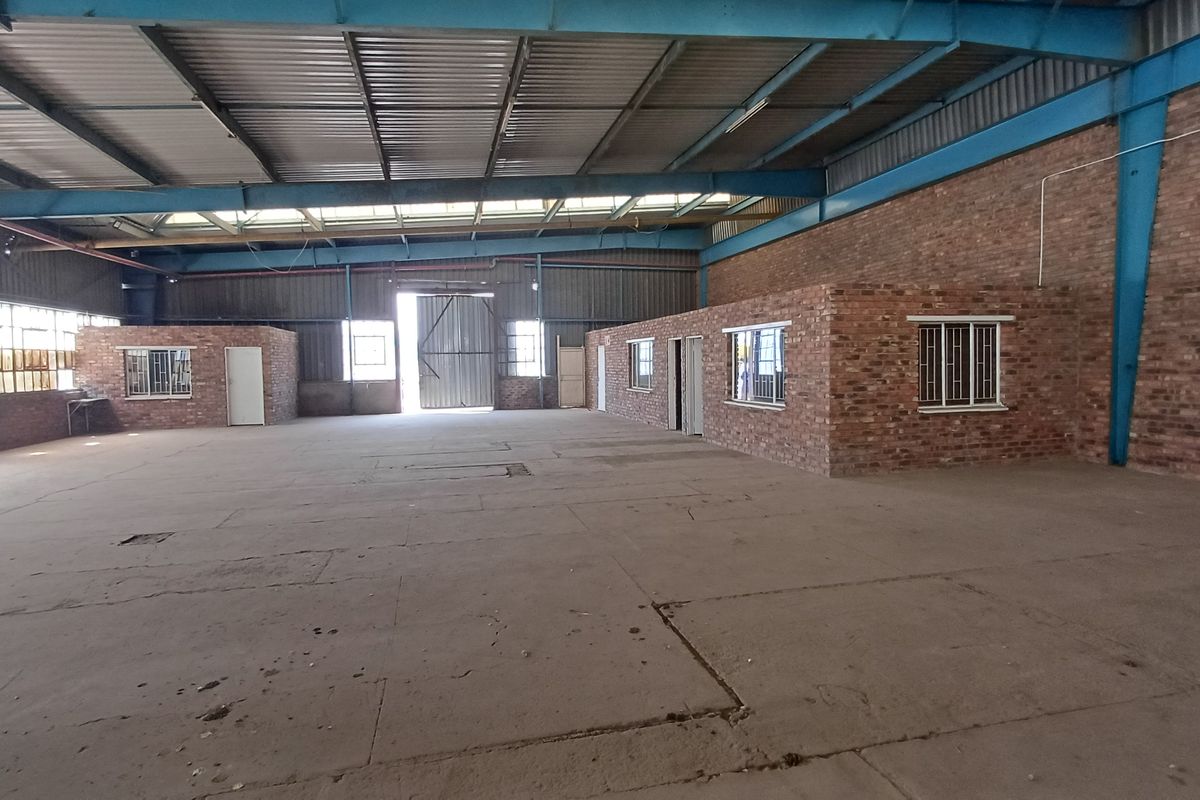 Spacious industrial warehouse featuring exposed steel roof trusses, concrete flooring, and internal brick-built office or utility rooms with secure window bars.