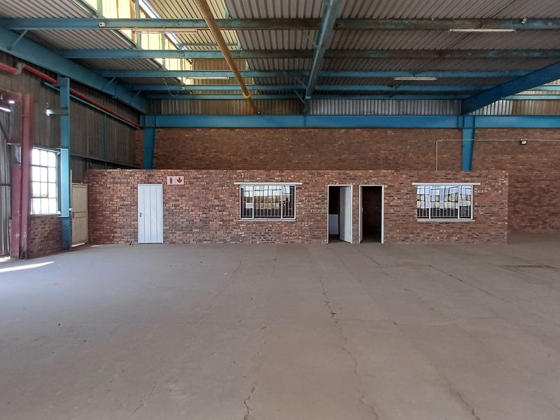 Spacious industrial warehouse featuring exposed steel roof trusses, concrete flooring, and internal brick-walled office or utility partitions.