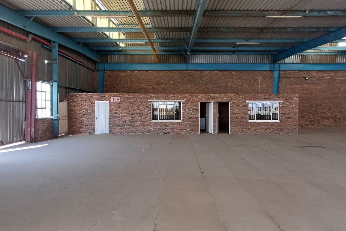 Spacious industrial warehouse featuring exposed steel roof trusses, concrete flooring, and internal brick-walled office or utility partitions.
