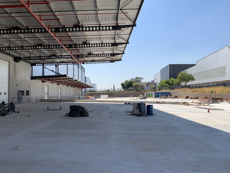 Large industrial loading yard featuring a covered canopy, concrete hardstand, and multiple roller shutter doors, suitable for logistics or manufacturing operations.
