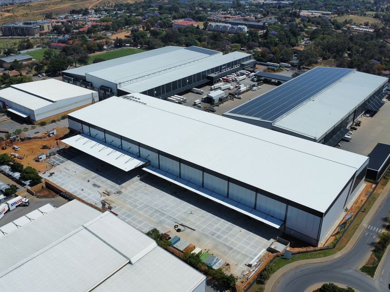 Aerial view of a large industrial warehouse complex featuring extensive concrete loading yards, metal roofing, and solar panel installations.