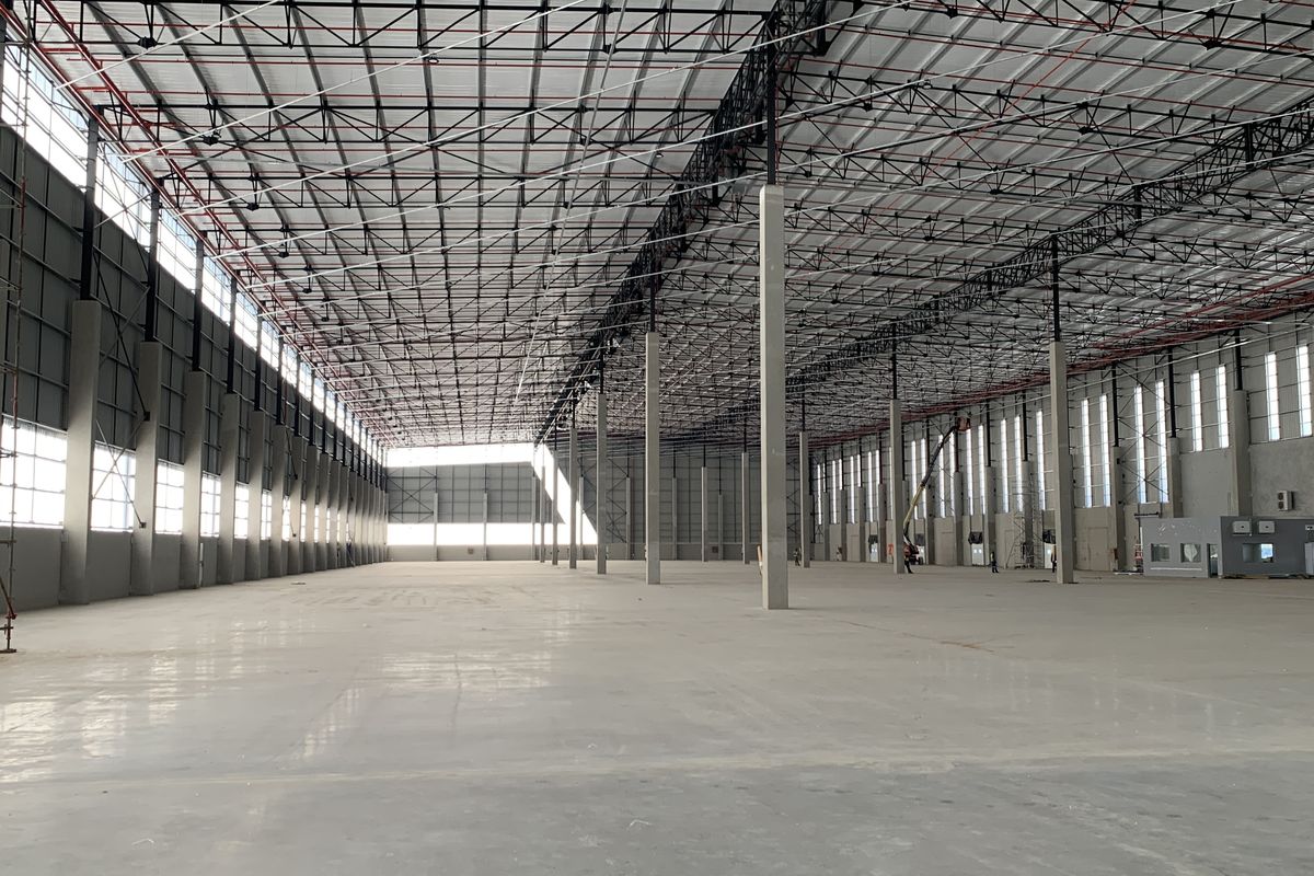 Expansive industrial warehouse space featuring high ceilings with exposed steel trusses, polished concrete flooring, and integrated fire sprinkler systems.