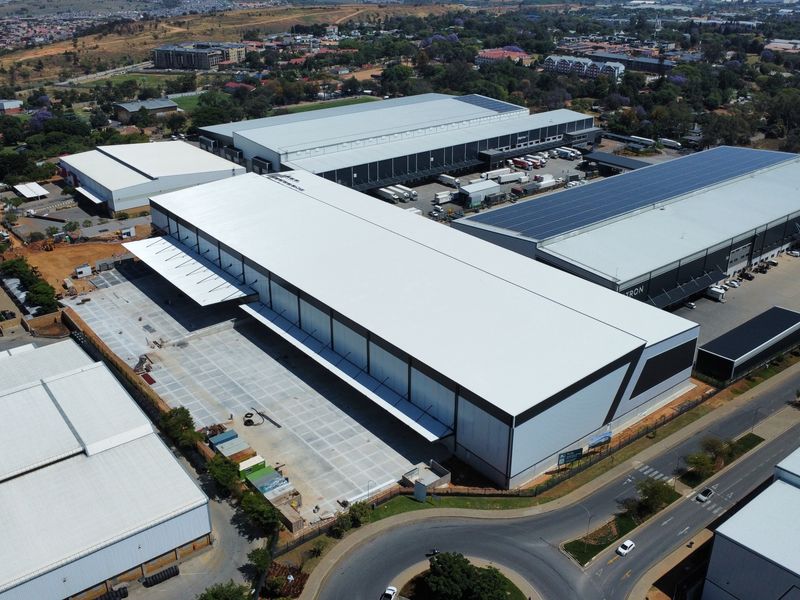 Aerial view of a large-scale industrial warehouse complex featuring extensive metal roofing, solar panels, and a spacious concrete loading yard.