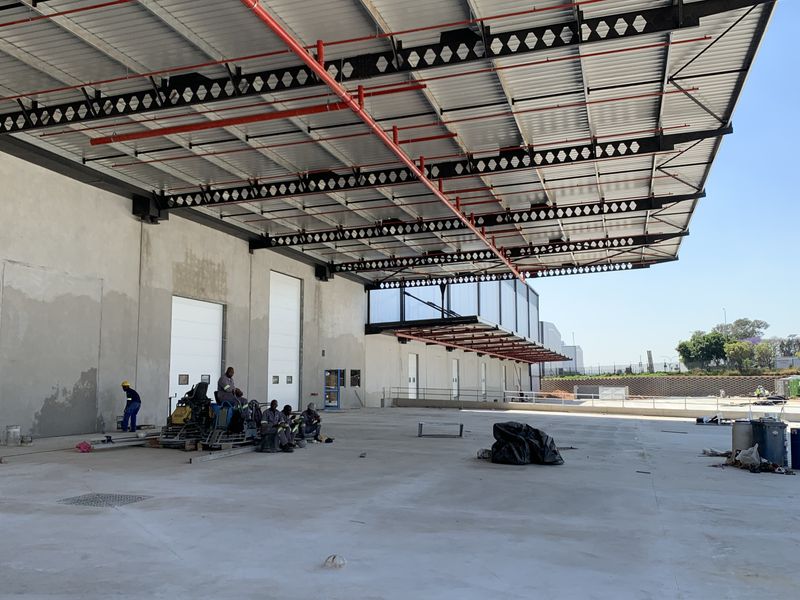 Large industrial loading bay area featuring a high-clearance steel portal frame, fire sprinkler system, and multiple roller shutter doors with concrete hardstand.