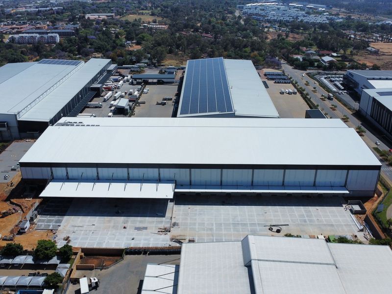 Aerial view of a large industrial warehouse facility featuring extensive solar panel installations, a spacious concrete loading yard, and multiple loading bays.