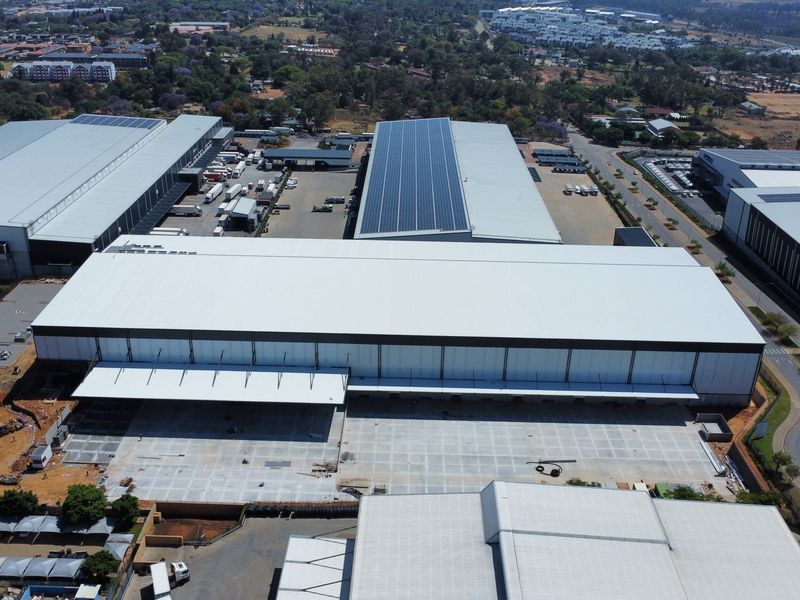 Aerial view of a large industrial warehouse complex featuring extensive metal roofing, solar panel installations, and a spacious concrete loading yard.