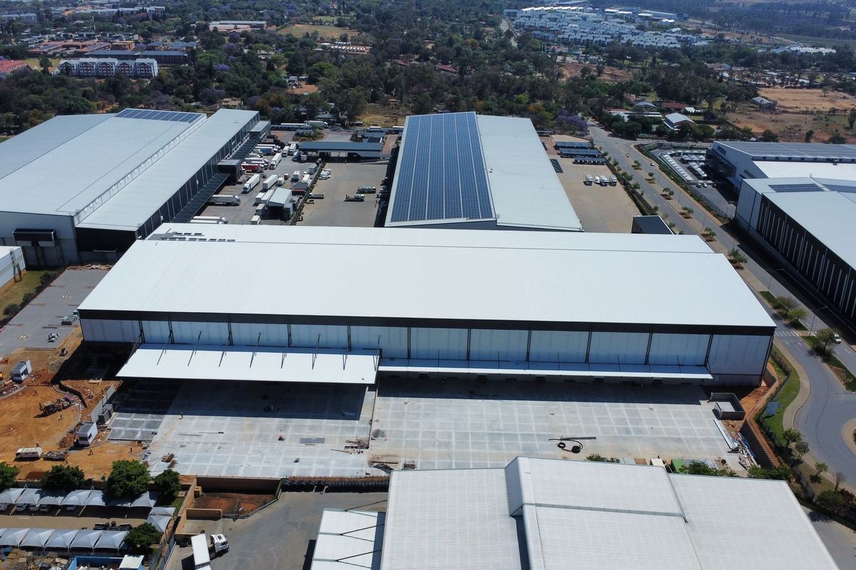 Aerial view of a large industrial warehouse complex featuring extensive metal roofing, solar panel installations, and a spacious concrete loading yard.