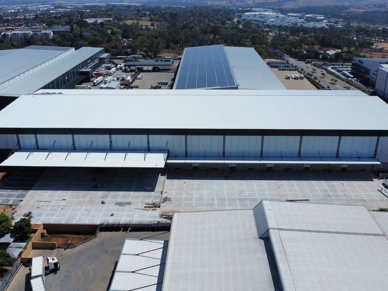 Aerial view of a large-scale industrial warehouse facility featuring extensive concrete loading yards, metal roofing, and integrated solar panel infrastructure.