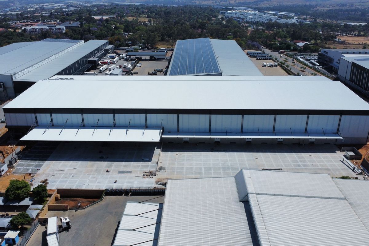 Aerial view of a large-scale industrial warehouse facility featuring extensive concrete loading yards, metal roofing, and integrated solar panel infrastructure.