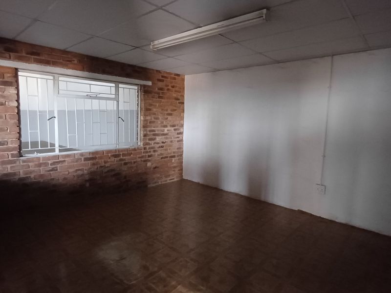 An empty industrial office space featuring exposed brickwork, tiled flooring, and a drop ceiling with integrated lighting.