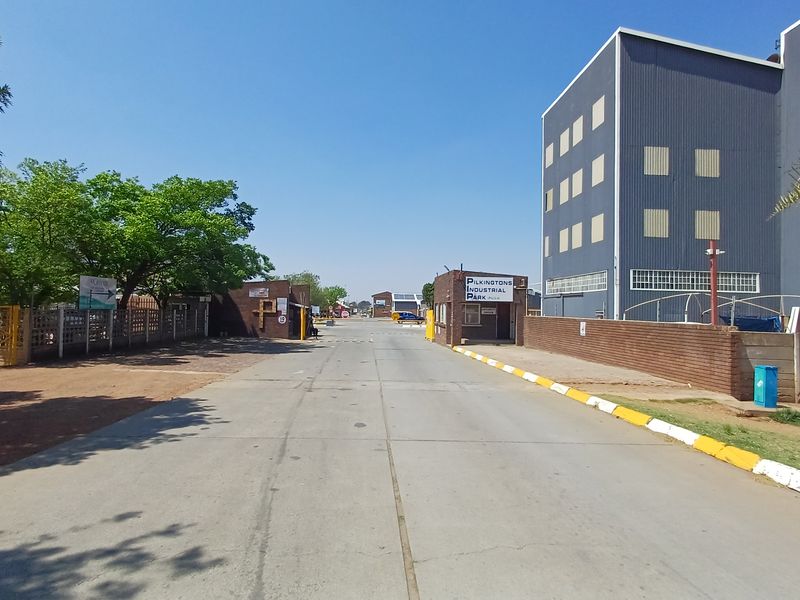 View of the entrance and access road to Pilkingtons Industrial Park, featuring security infrastructure and large-scale industrial warehouse buildings.