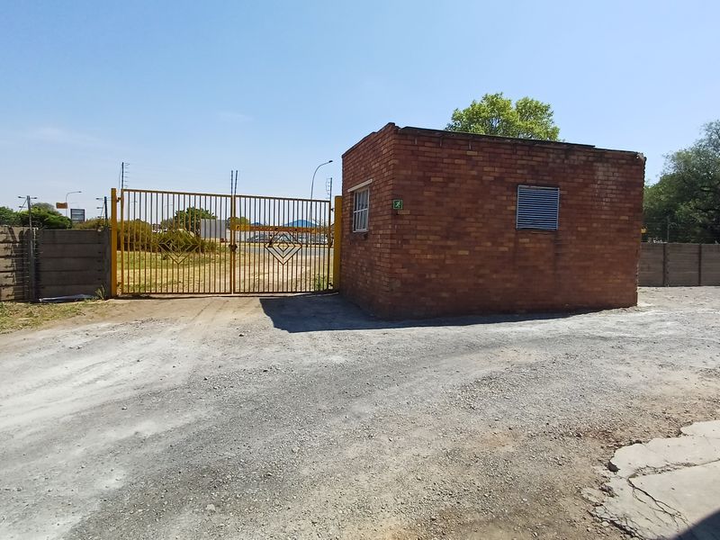 Industrial property entrance featuring a brick security guard house, metal gate, and precast concrete perimeter walling.