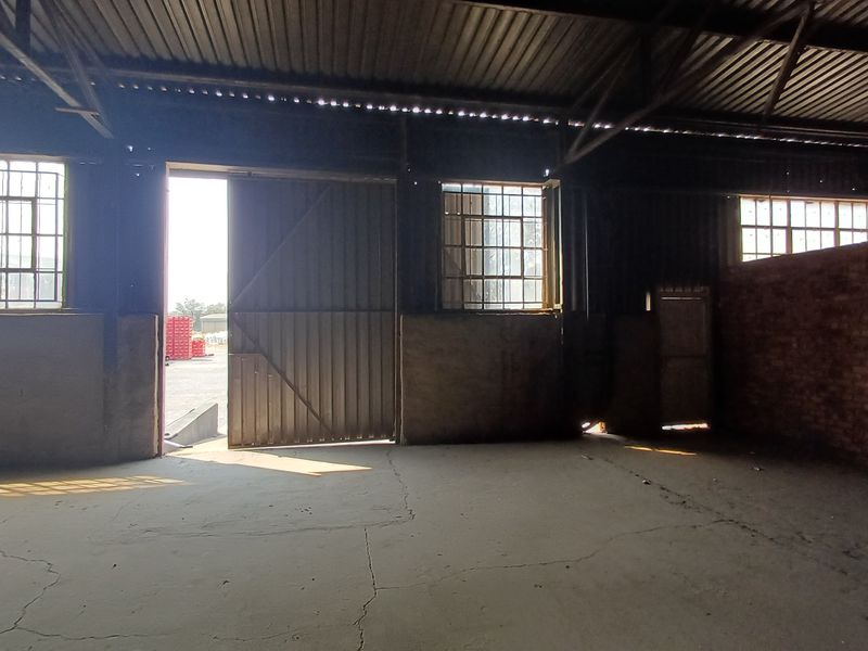 Spacious industrial utility area featuring exposed brickwork, steel-framed windows, and a large sliding door, offering a versatile open-plan workspace.
