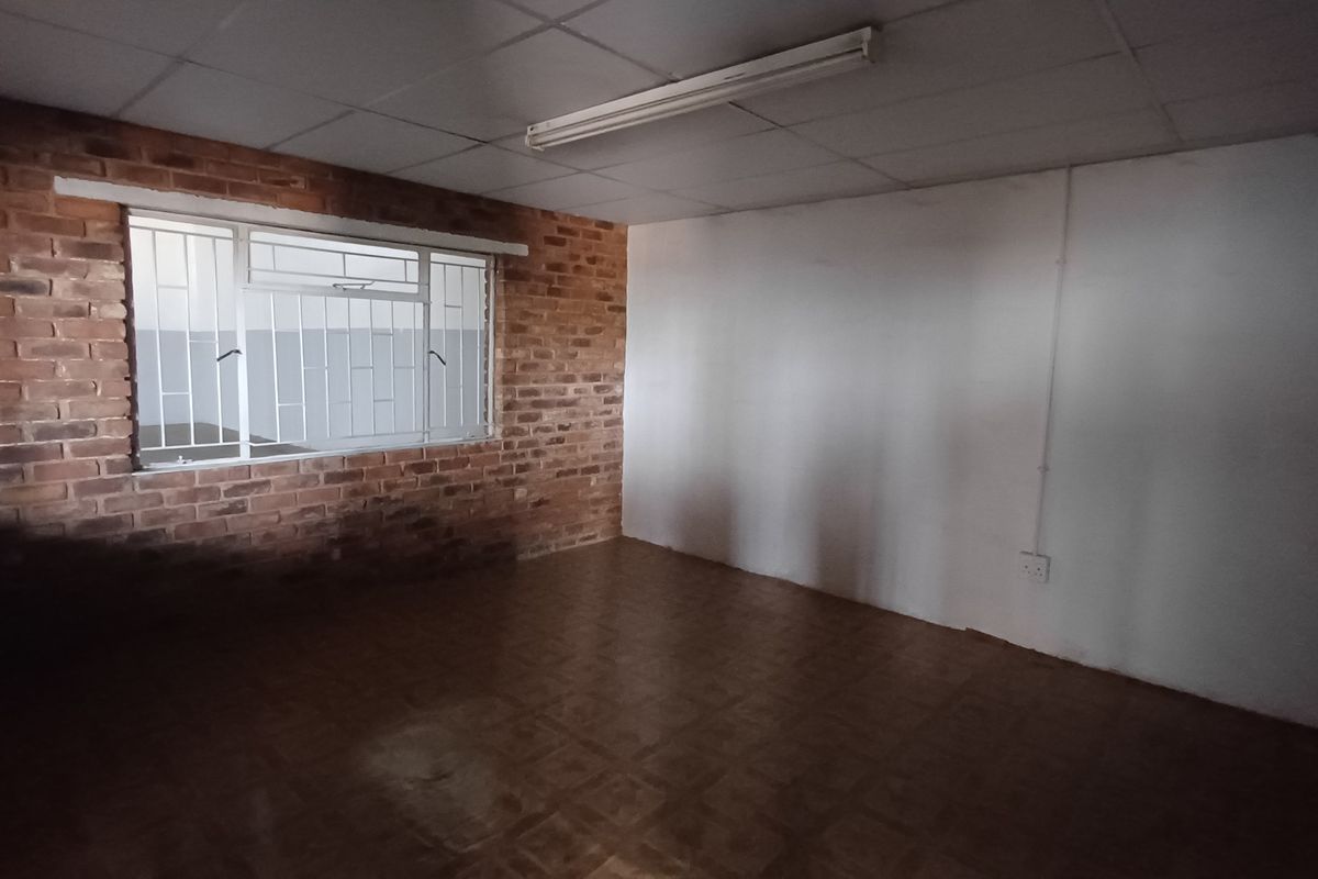 An empty industrial office space featuring exposed brickwork, tiled flooring, and a drop ceiling with integrated lighting.