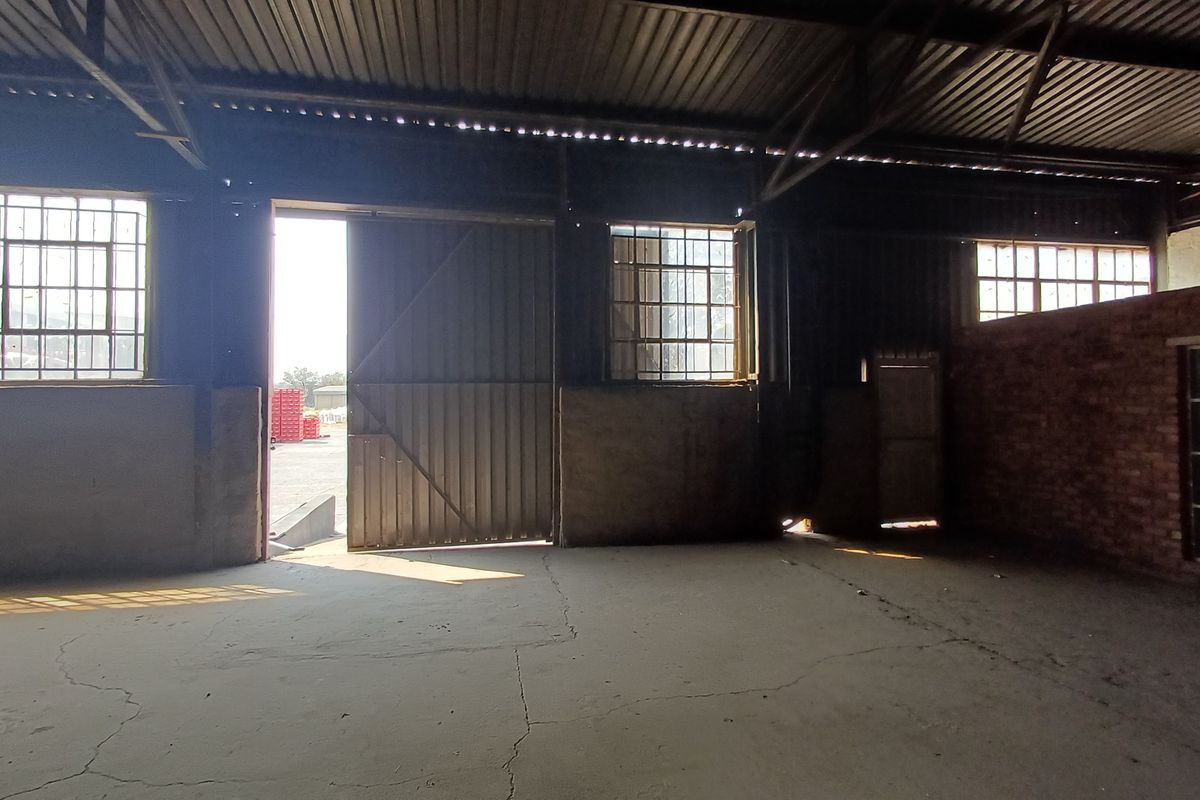 Spacious industrial utility area featuring exposed brickwork, steel-framed windows, and a large sliding door, offering a versatile open-plan workspace.