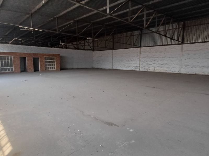 Spacious industrial warehouse featuring exposed steel roof trusses, concrete flooring, and an integrated brick office structure, suitable for various commercial or storage applications.