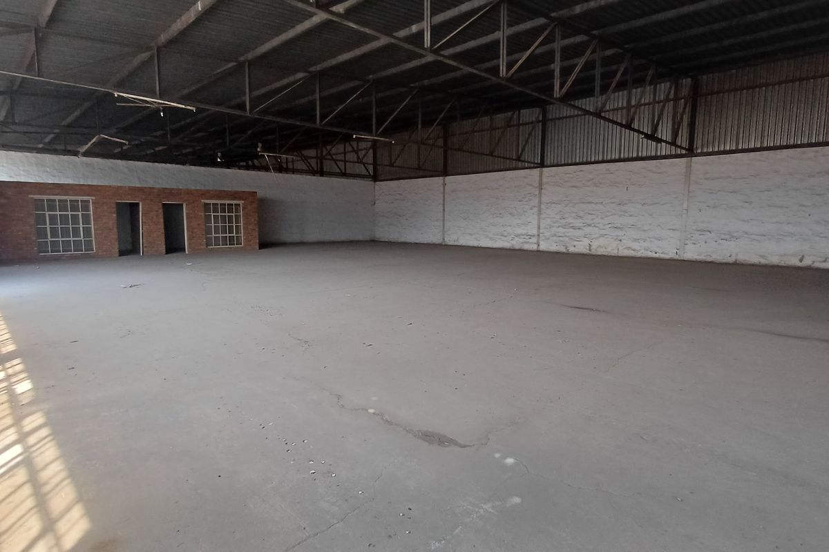 Spacious industrial warehouse featuring exposed steel roof trusses, concrete flooring, and an integrated brick office structure, suitable for various commercial or storage applications.