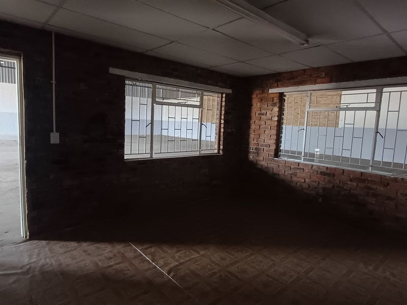 An empty industrial office space featuring exposed brick walls, security bars on windows, and a suspended ceiling with fluorescent lighting.