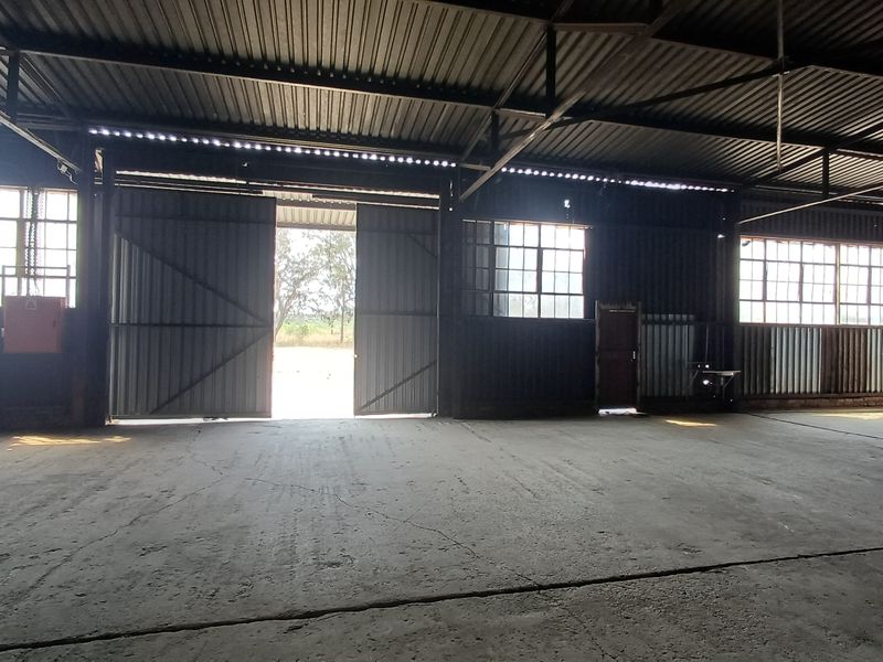 Spacious industrial utility area featuring high ceilings, exposed steel trusses, large sliding access doors, and durable concrete flooring.