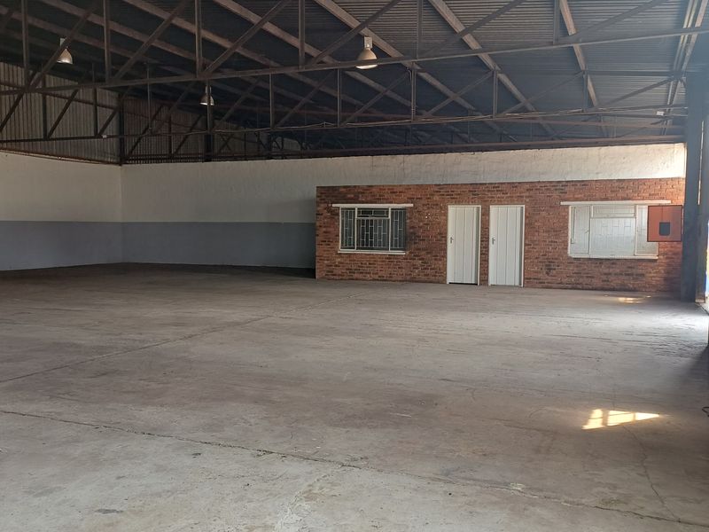 Spacious industrial warehouse featuring high ceilings with exposed steel trusses, concrete flooring, and an integrated internal office block with brick finish.