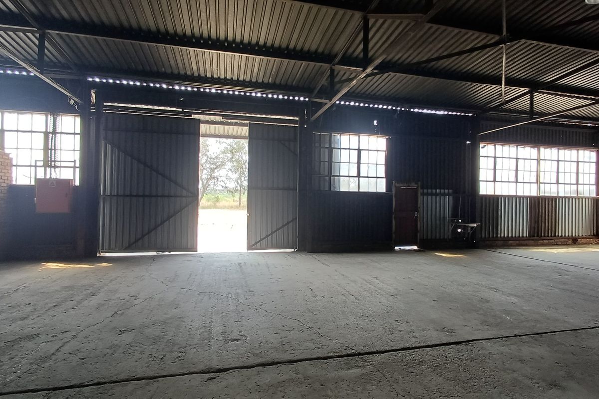 Spacious industrial utility area featuring high ceilings, exposed steel trusses, large sliding access doors, and durable concrete flooring.