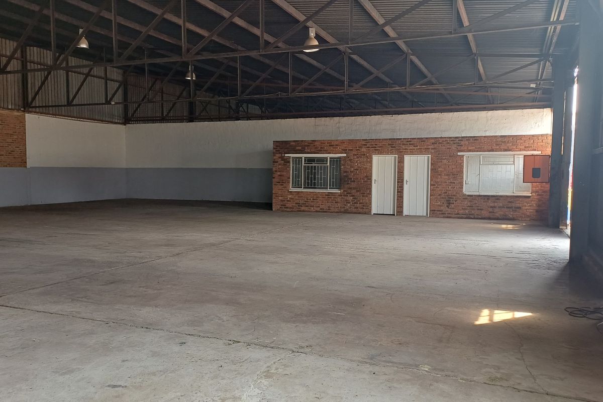 Spacious industrial warehouse featuring high ceilings with exposed steel trusses, concrete flooring, and an integrated internal office block with brick finish.