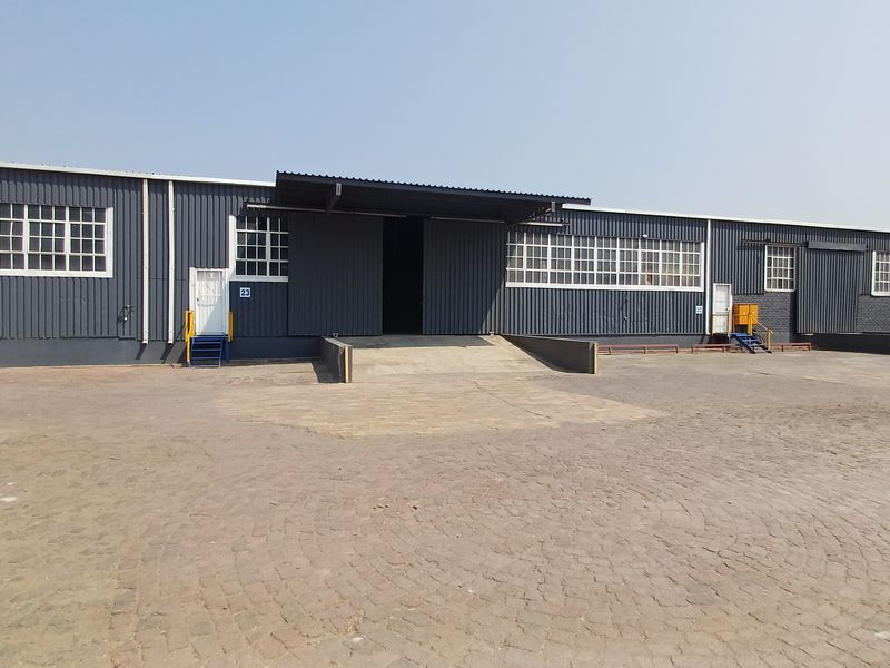 Industrial warehouse exterior featuring corrugated metal cladding, multiple loading bays with ramps, and large steel-framed windows, set within a spacious paved yard.