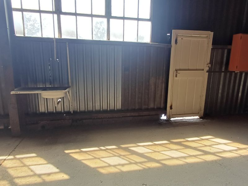 Industrial utility space featuring corrugated metal walls, concrete flooring, a wall-mounted sink, and large steel-framed windows providing natural light.
