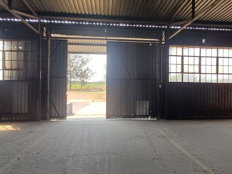 Spacious industrial utility area featuring high corrugated metal ceilings, large steel-framed windows, and expansive sliding doors opening to the exterior.